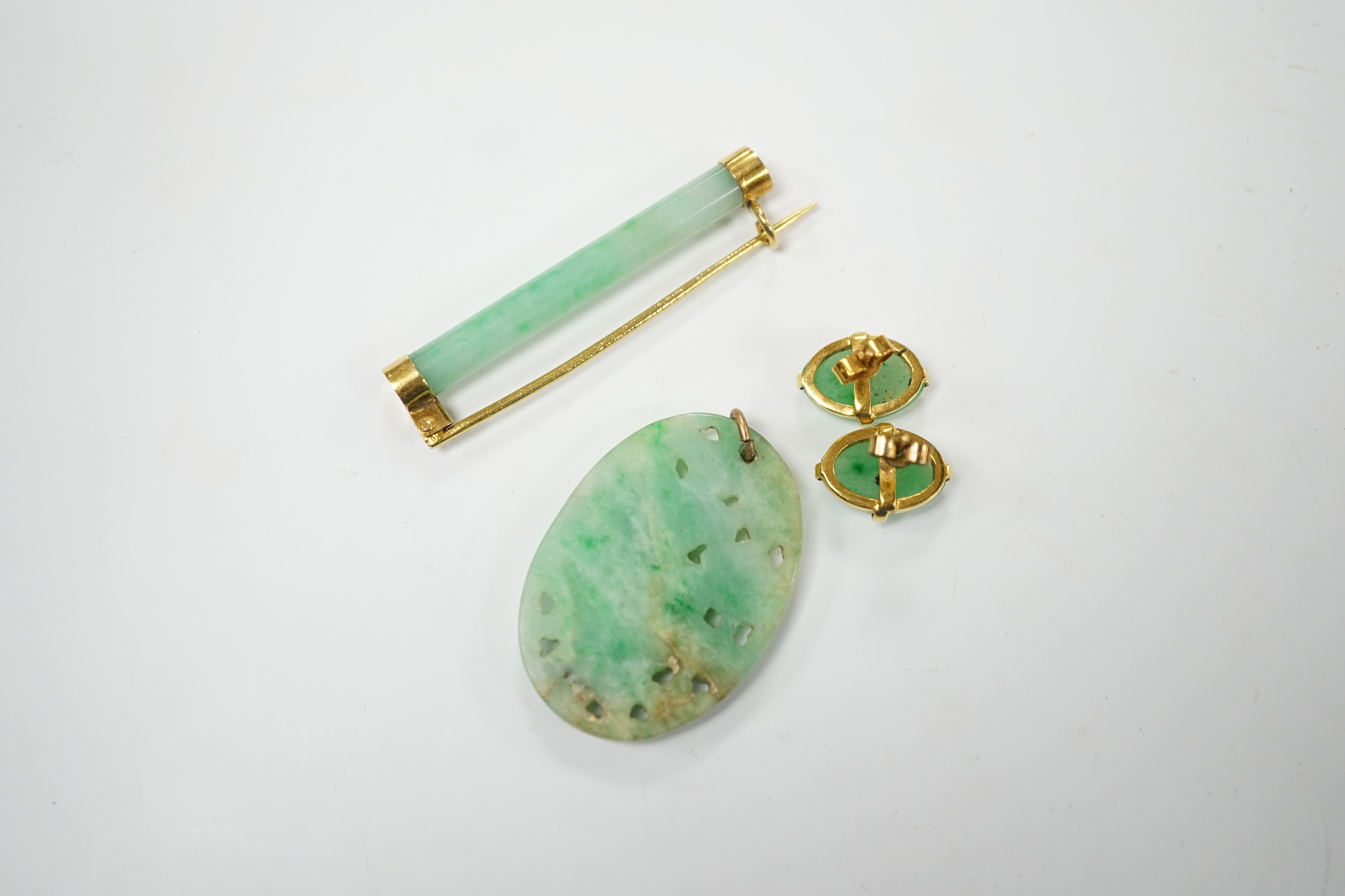 A Chinese yellow metal(stamped 18) mounted jade bar brooch, 48mm, a carved jade pendant and a pair of yellow metal mounted oval jade earrings, gross weight 19.9 grams. Fair to good condition.